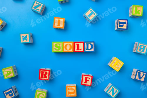 Preview: Sold. Wooden colorful alphabet blocks on blue background, flat lay, top view