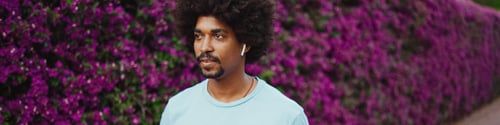 Preview: man listening to music in wireless headphones on background wall covered with purple flowers