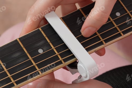 Preview: Female fingers applying capodastro to six string acoustic classical guitar