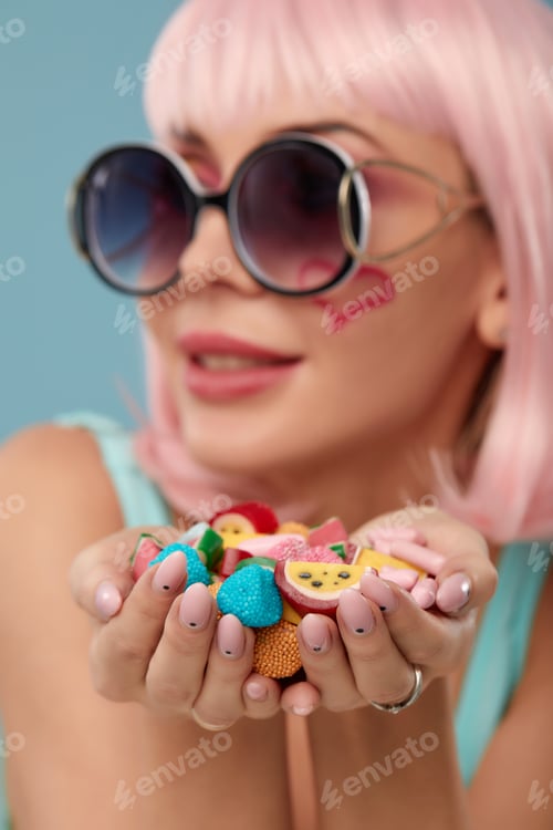 Preview: Close up of a flirtatious female model on blue background wearing a pink wig holding different kinds