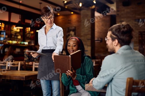 Preview: Happy waitress recommending an order from a menu to her customers in a pub.