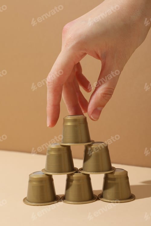 Preview: Golden coffee capsules and hand on beige background