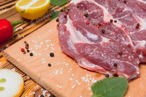 Preview: Raw pork meat with spices and vegetables on wooden table.