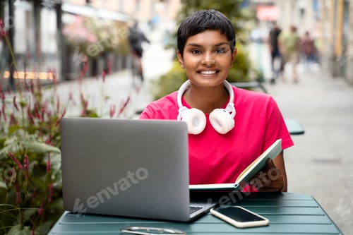 Preview: Indian woman freelancer using laptop computer, working online looking at camera at workplace