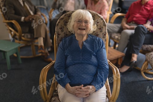 Preview: Front view of happy senior woman with hand clasped, sitting and looking at camera in nursing home