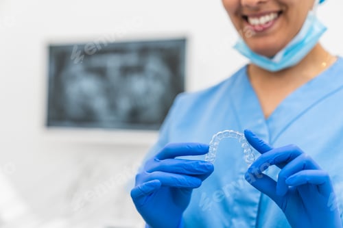 Preview: Close-up of a smiling dental hygienist holding a clear retainer during an orthodontic checkup.