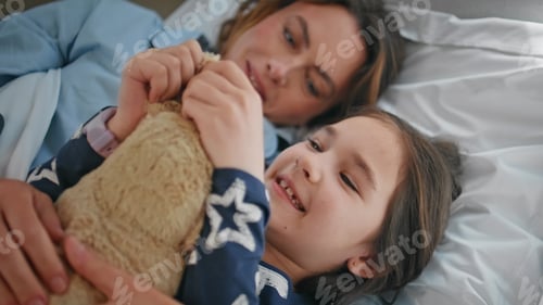 Preview: Small girl playing toy resting bedroom with mom closeup. Mother daughter lying
