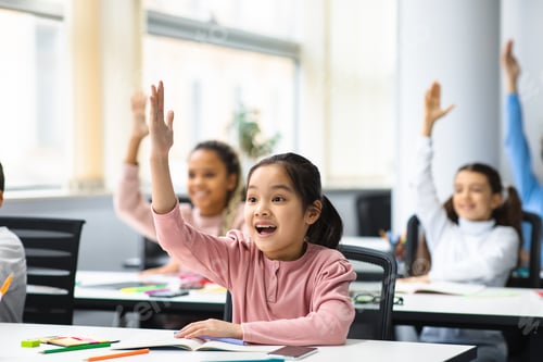 Preview: Diverse small schoolchildren raising hands at classroom