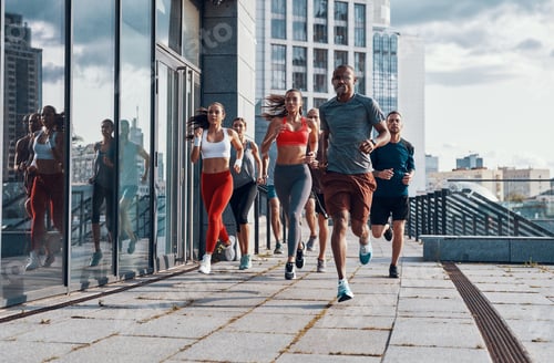 Preview: Full length of people in sports clothing jogging while exercising on the sidewalk outdoors