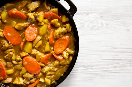 Preview: Homemade Japanese Chicken Curry in a cast-iron pan on a white wooden background, top view.