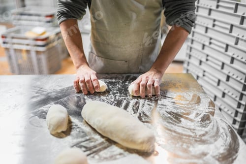 Preview: Baker kneading dough on stainless steel table in bakery