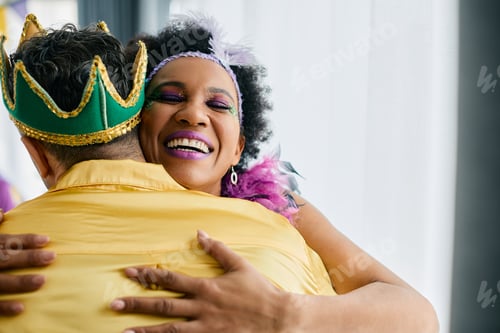 Preview: Happy black woman embracing her friend while celebrating Mardi Gras at home.