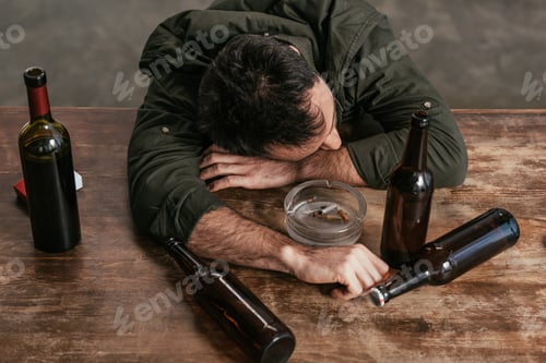 Preview: High angle view of drunk man lying on table with bottles and ashtray