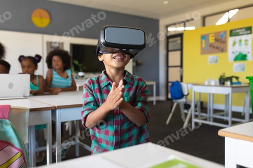 Preview: Smiling african american elementary schoolboy wearing vr glasses while standing in classroom