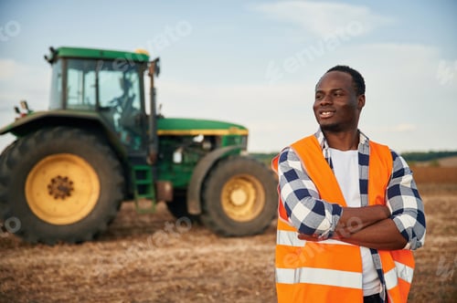Preview: Near the tractor in orange uniform. Beautiful African American man is in the agricultural field
