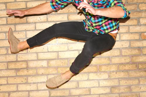 Preview: A cropped shot of a young man jumping with two feet through the frame in front of a brick wall
