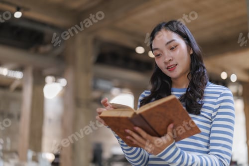 Preview: Young woman reading a book in a modern library