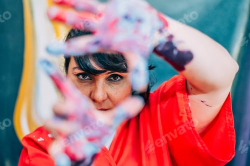 Preview: Woman artist framing creative vision with paint covered hands