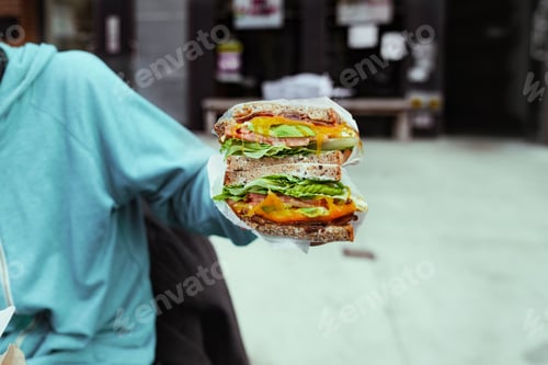 Preview: Man holding big portion sandwich outside closeup