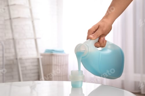 Preview: Woman pouring detergent into cap on table indoors, closeup with space for text. Laundry day
