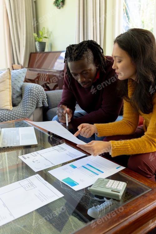 Preview: Focused diverse couple sitting on couch discussing bills and domestic finances in living room