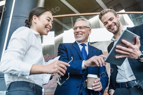 Preview: Low angle view of group successful business people in suits using digital tablet indoor