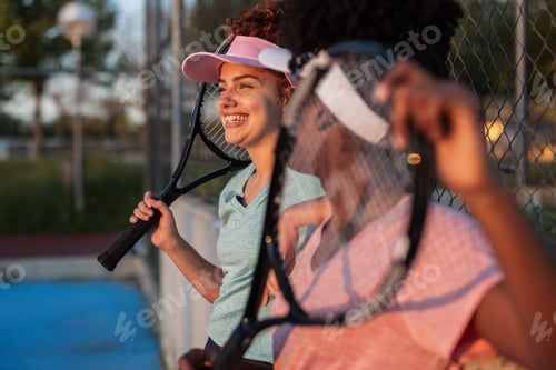 Preview: Two happy female tennis players resting after match at sunset