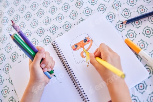 Preview: Crop kid drawing picture in notepad at table