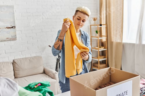 Preview: volunteering and charity, trendy and tattooed woman standing with yellow jumper near carton box