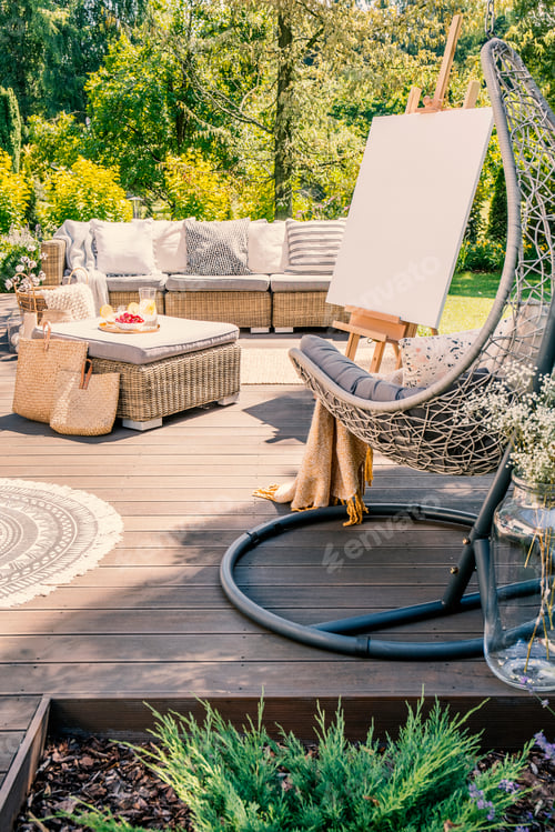 Preview: Hanging chair on wooden patio with easel and rattan table in fro