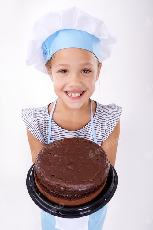Preview: Studio shot of a cute young girl wearing a chefs hat and holding up a chocolate cake