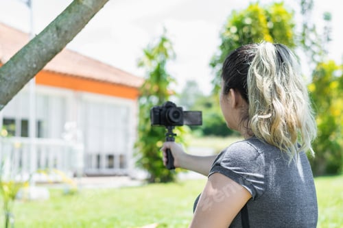 Preview: view of the back of a blogger girl filming herself with a camera in her hand in a green park