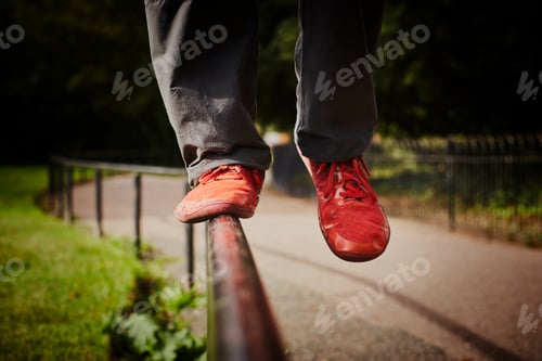 Preview: Man training in park, legs and red trainers balancing on fence