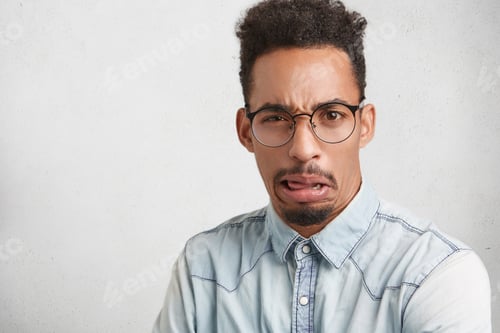 Vista previa: Waist up portrait of fashionable bearded male wears glasses and shirt, has disgusted expression as s