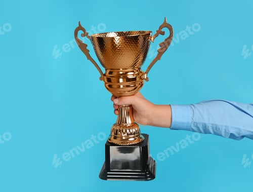 Preview: Boy holding golden winning cup on blue background, closeup