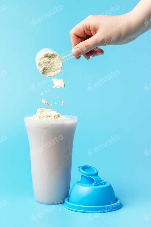 Preview: Female hand pours Shaker protein on blue background, side view.