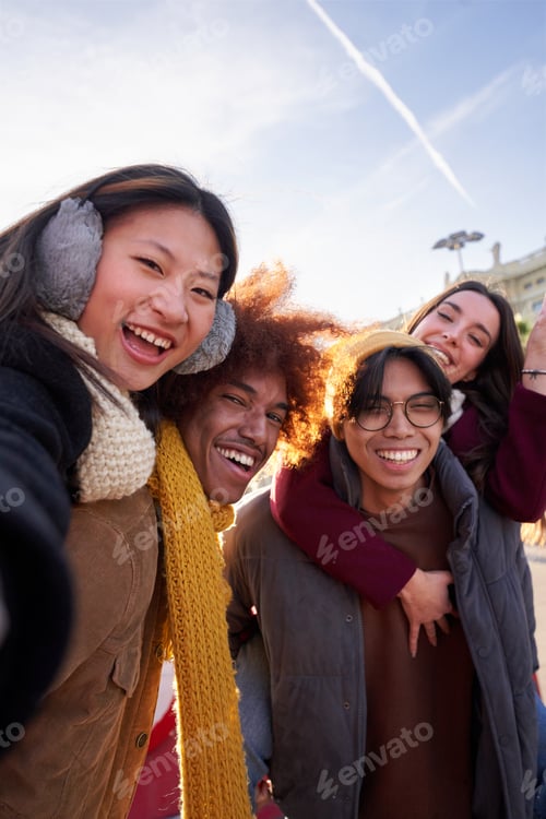 Preview: Happy selfie of group of four international friends doing piggyback outside at city at winter time.