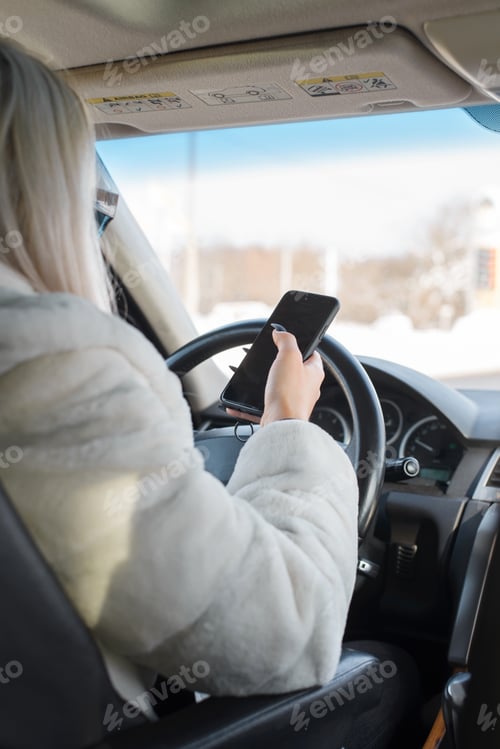 Preview: Young woman sitting in the car and using the phone while driving. View from behind. Selective focus