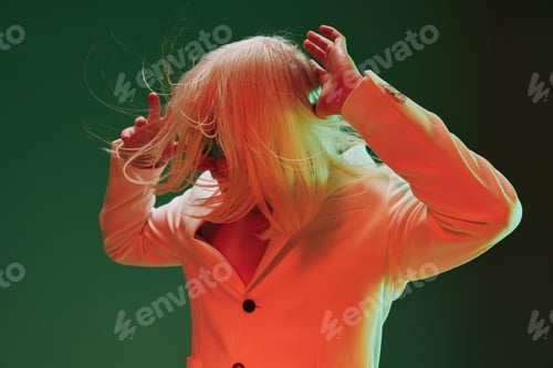 Preview: A person with long, light colored hair, dressed in a stylish blazer, poses dramatically against a