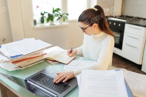 Preview: A woman with glasses on her job, utilizing her laptop and managing documents efficiently in a home