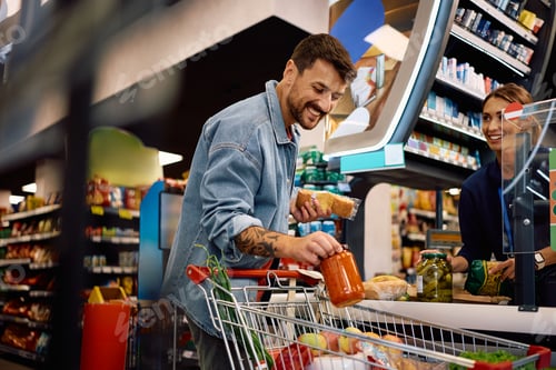Preview: Happy man paying for groceries at cash register in a supermarket.