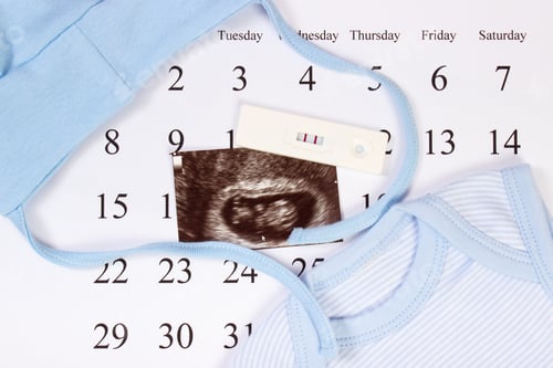 Preview: Pregnancy test, ultrasound scan of baby and blue clothing for newborn on calendar