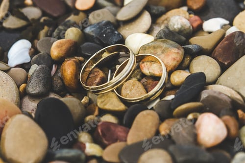 Preview: Gold wedding rings on the rocks of a beach.
