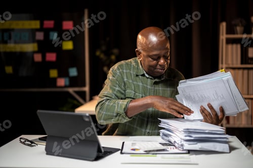 Preview: A man is sitting at a desk with a stack of papers in front of him
