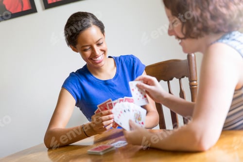 Preview: Angled view of young women sitting at dining table playing cards smiling