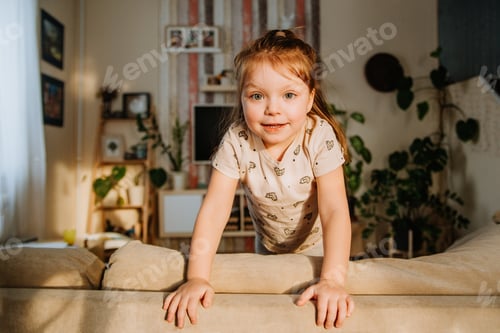 Preview: a little girl is standing on the couch in the living room and smiling