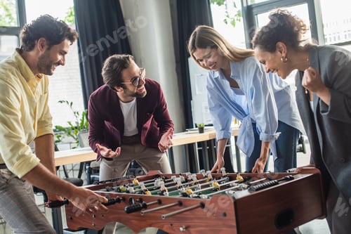 Preview: Excited interracial business people playing table soccer in office