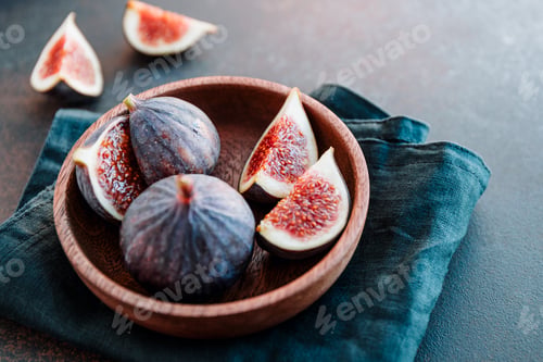 Preview: Top view of ripe quartes figs in a wooden small bowl on a table.