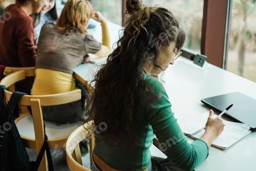 Preview: Young group of students studying inside university library - Focus on right girl hand