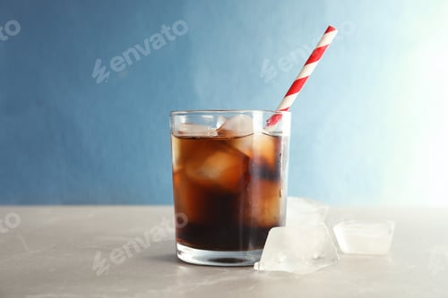 Preview: Glass of refreshing cola with ice on table against color background